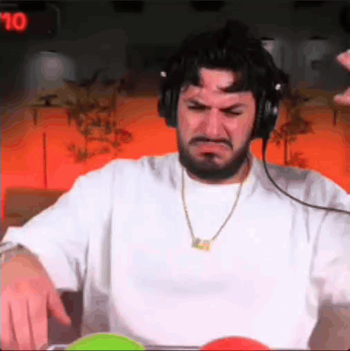 A Man With A Beard Wearing Headphones And A Necklace Is Making A Face . GIF
