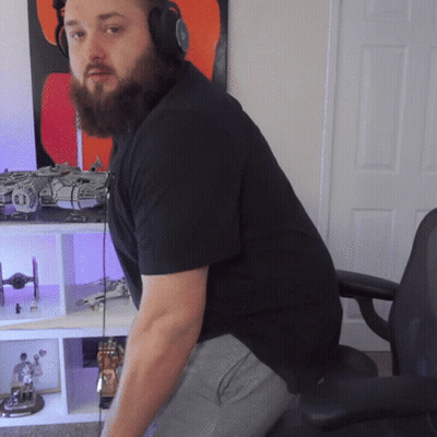 A Man With A Beard Wearing Headphones Is Sitting In Front Of A Shelf With Toys On It GIF