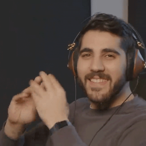 A Man With A Beard Wearing Headphones Is Smiling And Making A Heart Shape With His Hands . GIF