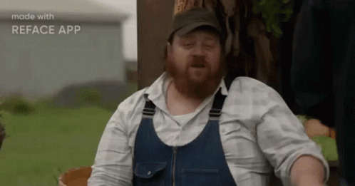 A Man With A Beard Wearing Overalls And A Hat Is Making A Funny Face . GIF