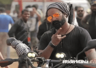 A Man With A Beard Wearing Sunglasses And A Beanie Is Giving The Middle Finger While Riding A Motorcycle . GIF