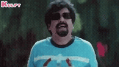 A Man With A Beard Wearing Sunglasses And A Blue Shirt Is Holding A Bottle Of Soda . GIF