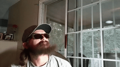 A Man With A Beard Wearing Sunglasses And A Hat Is Smoking A Cigarette GIF