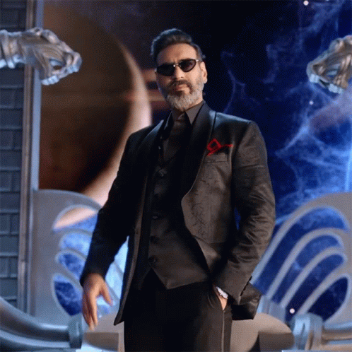 A Man With A Beard Wearing Sunglasses And A Suit Stands With His Hands In His Pockets GIF