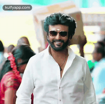 A Man With A Beard Wearing Sunglasses And A White Shirt Is Smiling In A Crowd . GIF