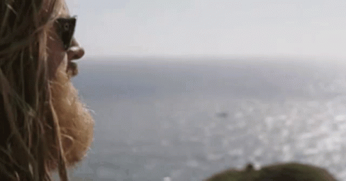 A Man With A Beard Wearing Sunglasses Looks Out Over The Ocean . GIF
