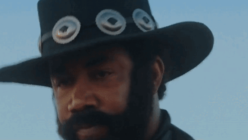 A Man With A Beard Wears A Cowboy Hat With Three Circles On It GIF