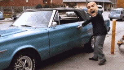 A Man With A Big Head Is Standing Next To A Blue Car With A Tire That Says Bfgoodrich On It GIF