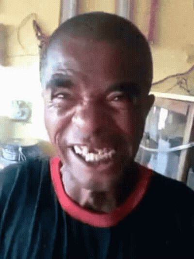 A Man With A Black Shirt And A Red Collar Is Smiling And Looking At The Camera . GIF