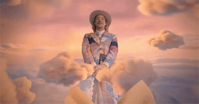 A Man With A Bow On His Head Stands Next To A Woman In A Yellow Dress GIF