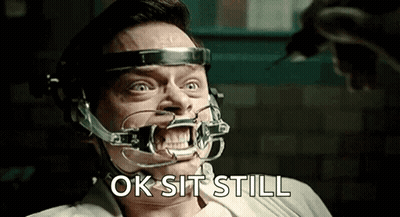 A Man With A Brace On His Teeth Is Sitting In A Chair And Says Ok Sit Still . GIF