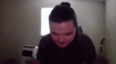 A Man With A Bun On His Head Is Standing In Front Of A Window In A Dark Room GIF