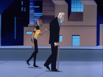 A Man With A Cane And A Woman With Pink Hair Walk Down A Street GIF