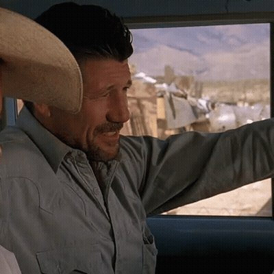 A Man With A Cowboy Hat On His Head Looks Out The Window GIF