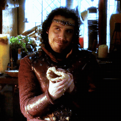 A Man With A Crown On His Head Is Holding A Pastry GIF