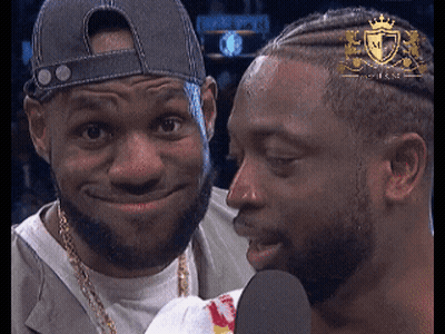 A Man With A Crown On His Head Talks Into A Microphone Next To Another Man GIF