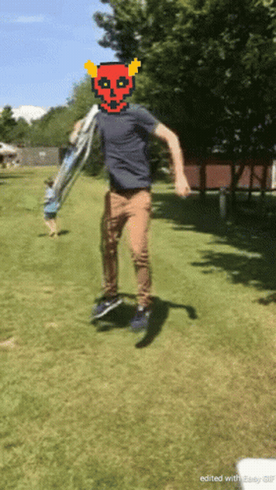 A Man With A Devil Mask On His Head Is Jumping In The Grass GIF