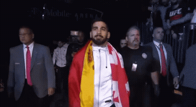 A Man With A Flag Around His Neck Walks Through A Crowd GIF