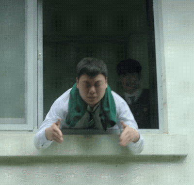 A Man With A Green Scarf Around His Neck Leans Out Of A Window GIF
