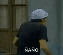 A Man With A Hat And A Mustache Is Standing In Front Of A Building . GIF