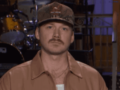 A Man With A Hat And A Mustache Is Wearing A Brown Shirt GIF