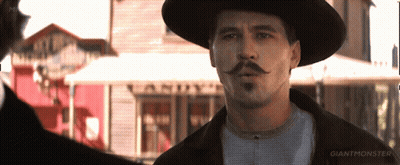 A Man With A Hat And Mustache Is Standing In Front Of A Building That Says Giant Monster GIF