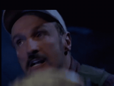 A Man With A Hat On Is Eating Popcorn In A Dark Room . GIF