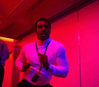 A Man With A Lanyard Around His Neck Is Running In A Room With Purple Lights GIF