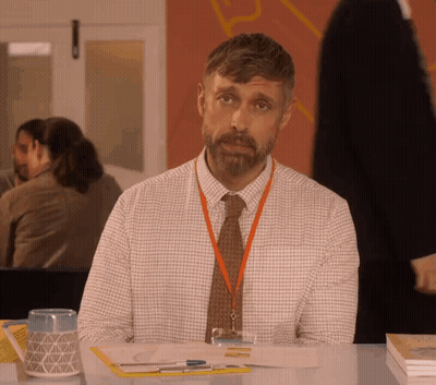 A Man With A Lanyard Around His Neck Sitting At A Desk GIF