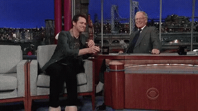 A Man With A Large Foot Is Sitting At A Table With A Man . GIF