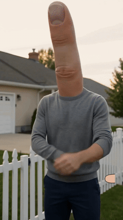 A Man With A Large Thumb On His Head Stands In Front Of A White Picket Fence GIF