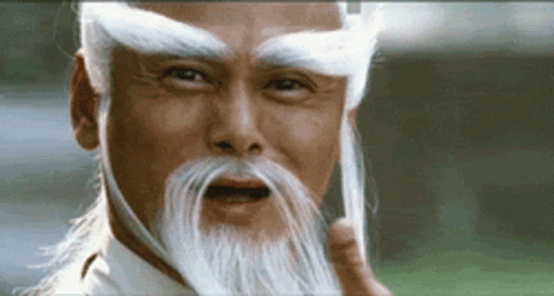 A Man With A Long White Beard And Eyebrows Is Making A Funny Face . GIF