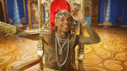 A Man With A Lot Of Tattoos Is Sitting In A Throne GIF