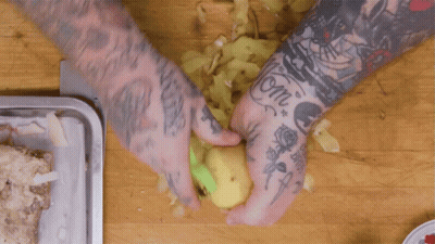 A Man With A Lot Of Tattoos On His Arms Is Peeling A Potato GIF