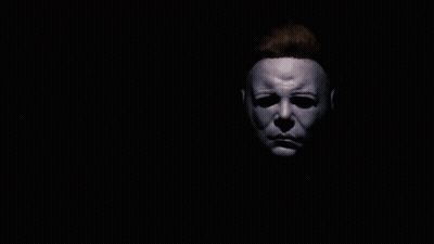 A Man With A Mask On His Face Holds His Hand Up In The Dark GIF