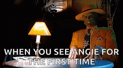 A Man With A Mask On His Face Is Sitting At A Table With A Lamp And Says When You See Angie For The First Time GIF