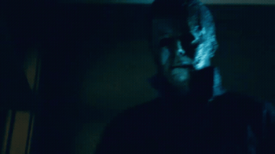 A Man With A Mask On His Face Is Standing In A Dark Room Looking At The Camera GIF