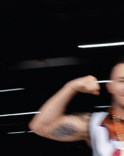 A Man With A Medal Around His Neck Flexes His Arm GIF