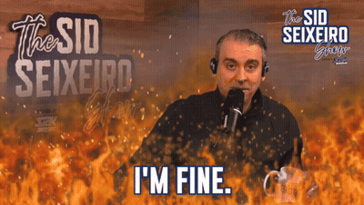 A Man With A Microphone Says I 'M Fine In Front Of A Fire Background GIF