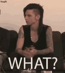 A Man With A Mohawk Is Sitting On A Couch With The Words `` What ? '' Written On It . GIF
