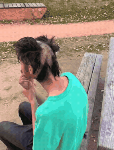 A Man With A Mohawk On His Head Sits On A Wooden Bench GIF