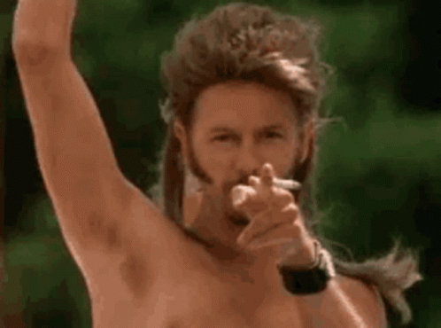 A Man With A Mullet And A Beard Is Smoking A Cigarette And Pointing At The Camera . GIF