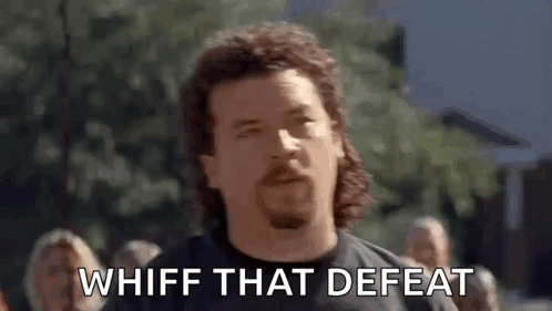 A Man With A Mullet And A Beard Is Standing In Front Of A Crowd And Saying Whiff That Defeat . GIF
