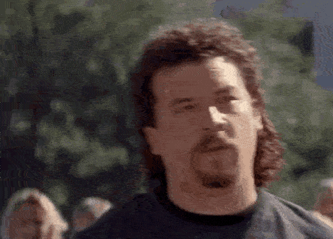 A Man With A Mullet And A Beard Is Wearing A Black Shirt . GIF