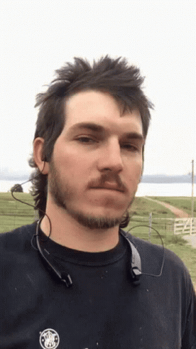 A Man With A Mullet And A Beard Is Wearing A Black Shirt GIF