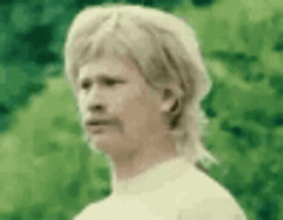 A Man With A Mullet And A Mustache Is Standing In Front Of A Green Background . GIF