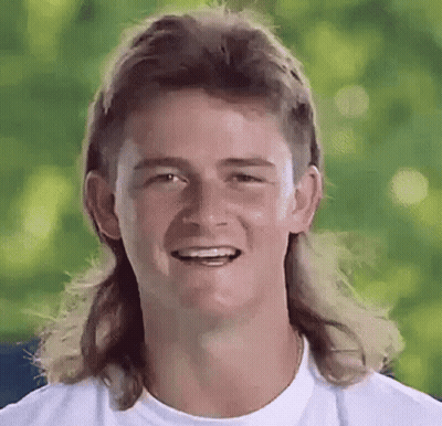 A Man With A Mullet And Long Hair Is Smiling . GIF