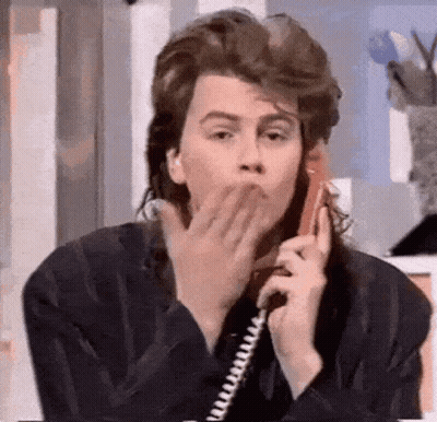 A Man With A Mullet Is Blowing A Kiss While Talking On A Phone . GIF