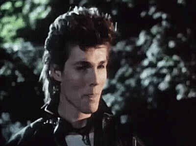 A Man With A Mullet Is Wearing A Black Leather Jacket And Looking At The Camera . GIF