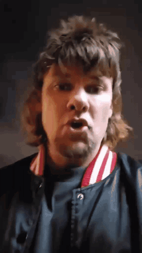 A Man With A Mullet Is Wearing A Blue Jacket With Red And White Stripes GIF